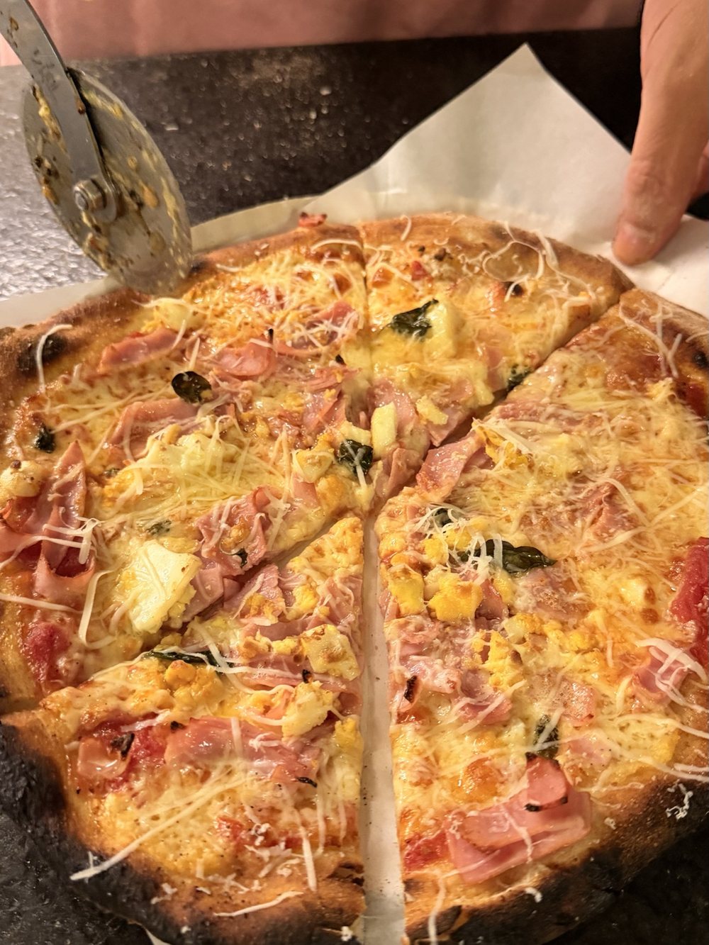 Pizza recém-assada sendo fatiada com cortador de roda
