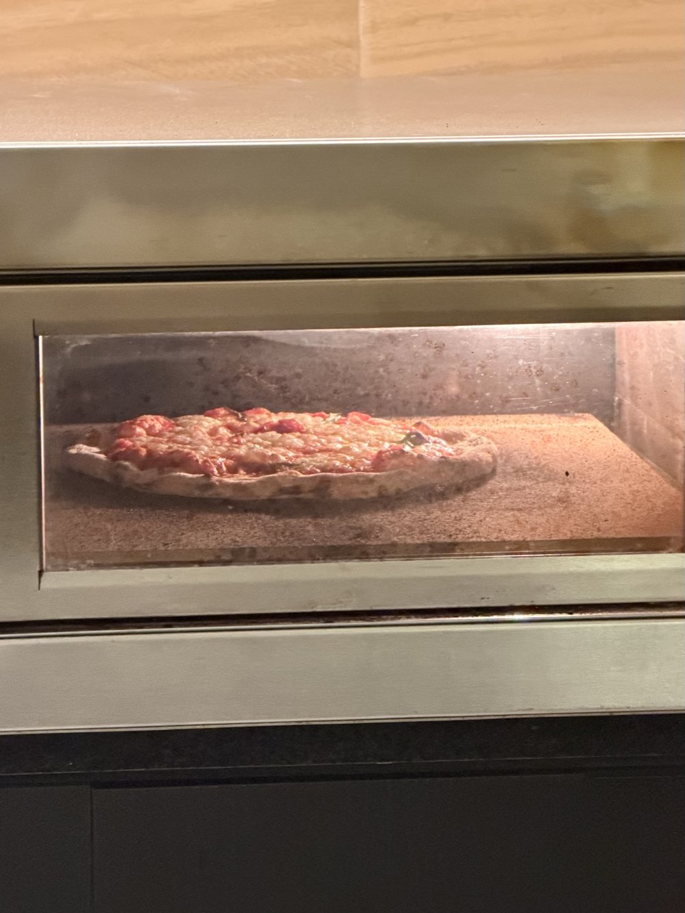Pizza assando dentro do forno, vista pelo vidro
