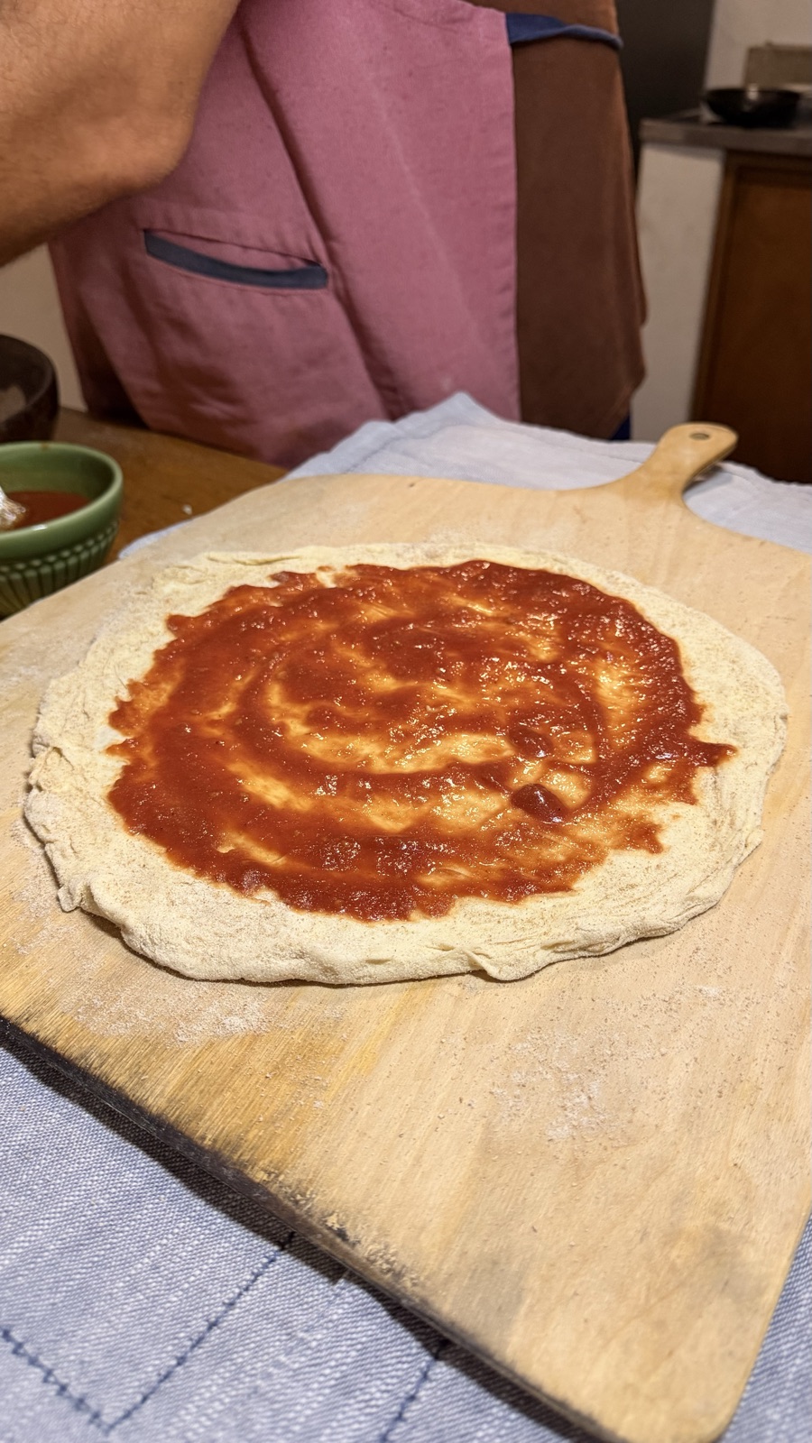Massa aberta recebendo molho de tomate na pá de madeira