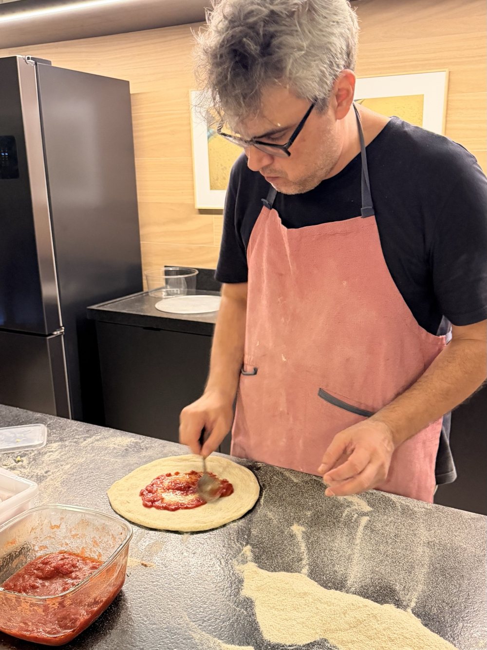 O pizzaiolo espalhando o molho de tomate sobre a massa na bancada