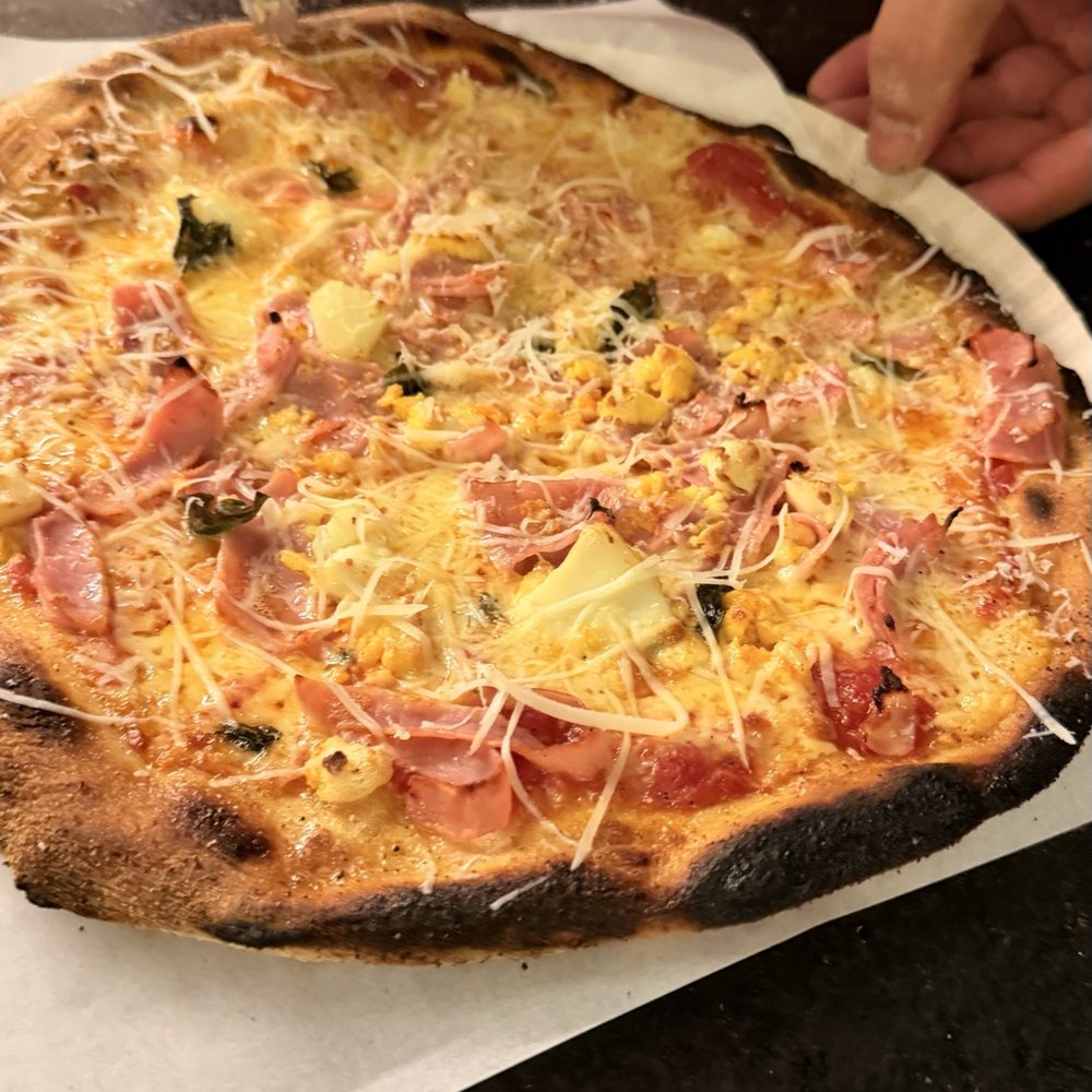 Pizza portuguesa de presunto, ovo e parmesão sendo servida
